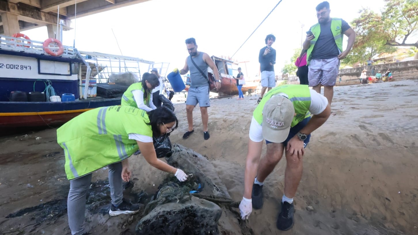 Pessoas recolhendo sacos de lixo na beira de um rio
